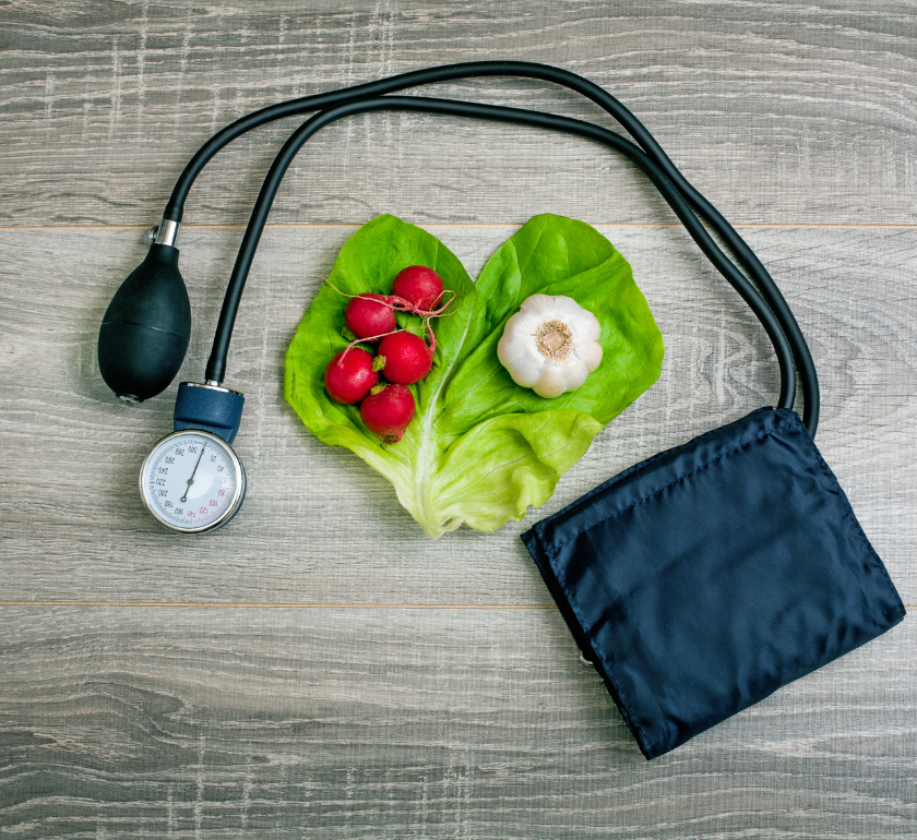 blood pressure cuff laying beside lettuce tomatoes and garlic