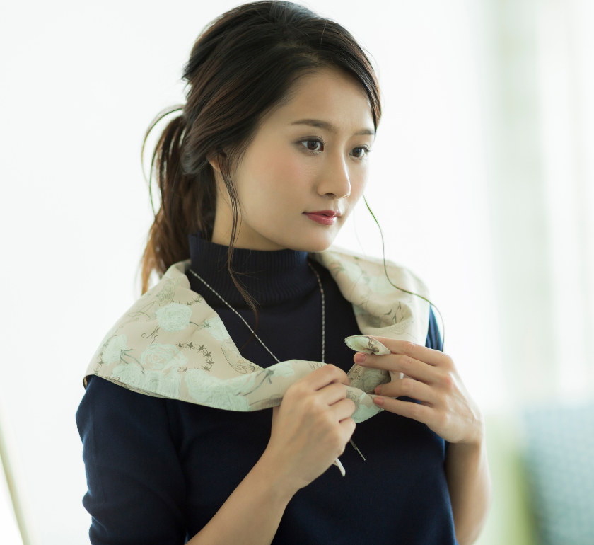 an asian woman adjusting her scarf and looking into the distance