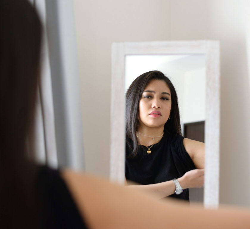 woman with body dysmorphia and negative body image pinching arms and looking in mirror at self