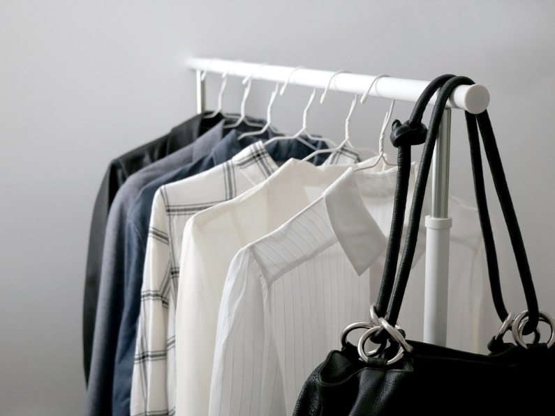 a minimalist capsule wardrobe with neutral colored shirts and a black purse on a white rolling rack