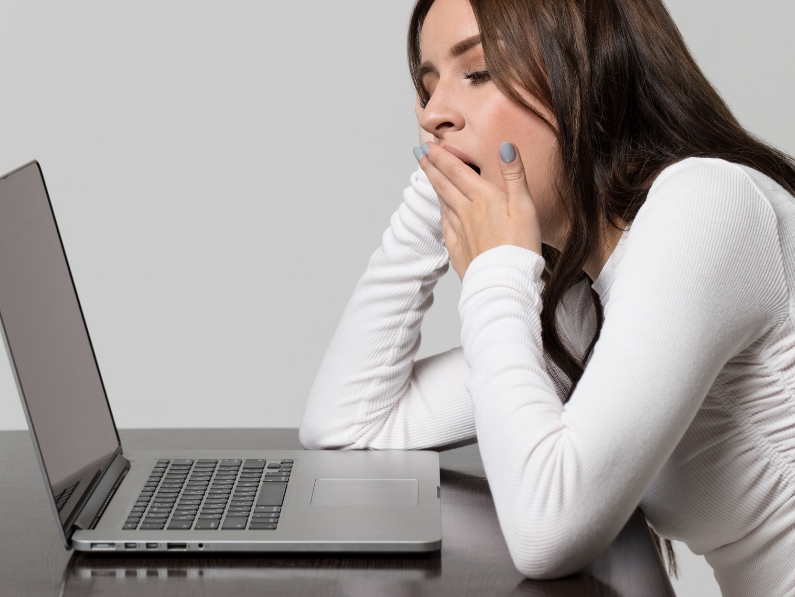 woman sitting at laptop yawning because of chronic fatigue